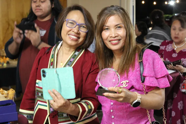 Two women laughing together at FIRM's awards night, one holding an engraved award plate.