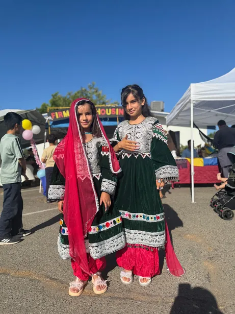 Two young women in bright embroidered dresses standing together at an outdoor FIRM festival.