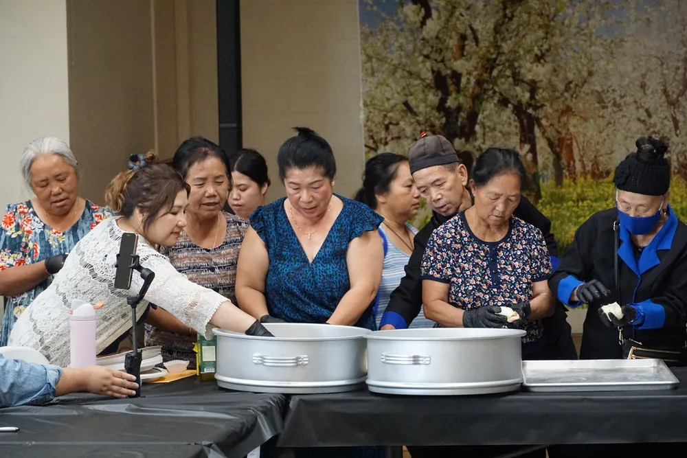 Elders standing around wide cooking pots at a FIRM community kitchen.