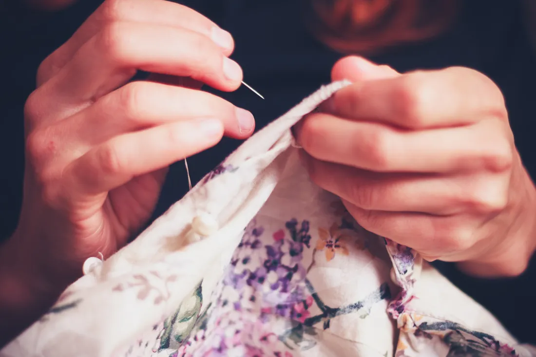 Close-up of two hands stitching a floral panel by hand at a FIRM sewing class.
