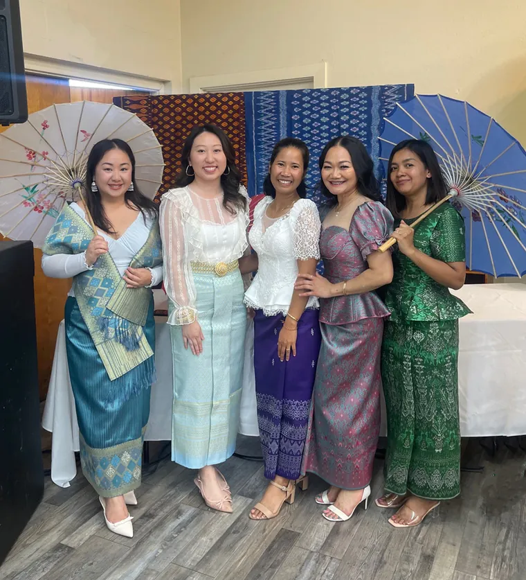 Five women in Lao and Thai dress holding painted parasols at a FIRM new year celebration.