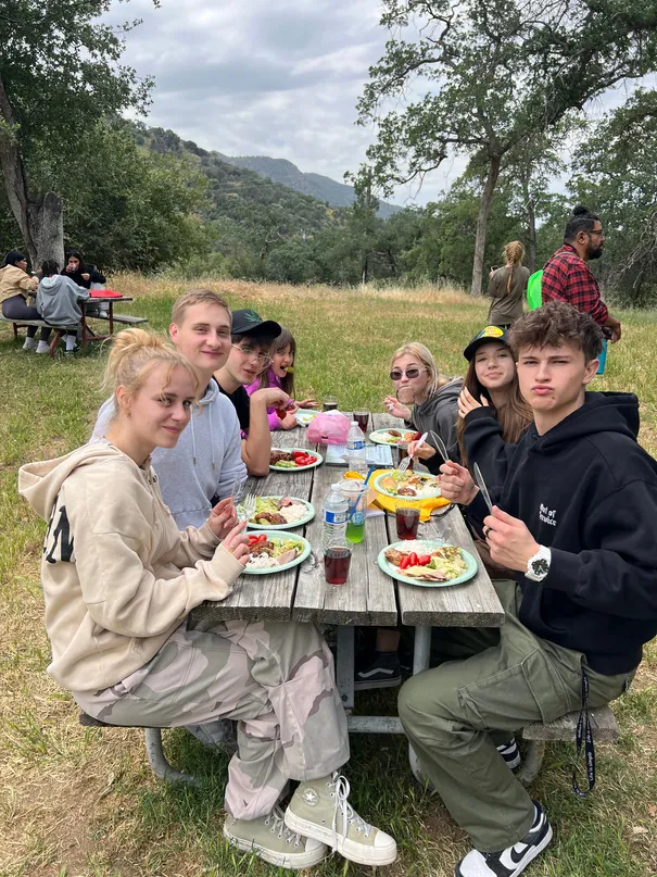 Young people from FIRM sitting at a picnic table with plates of food on a community trip.